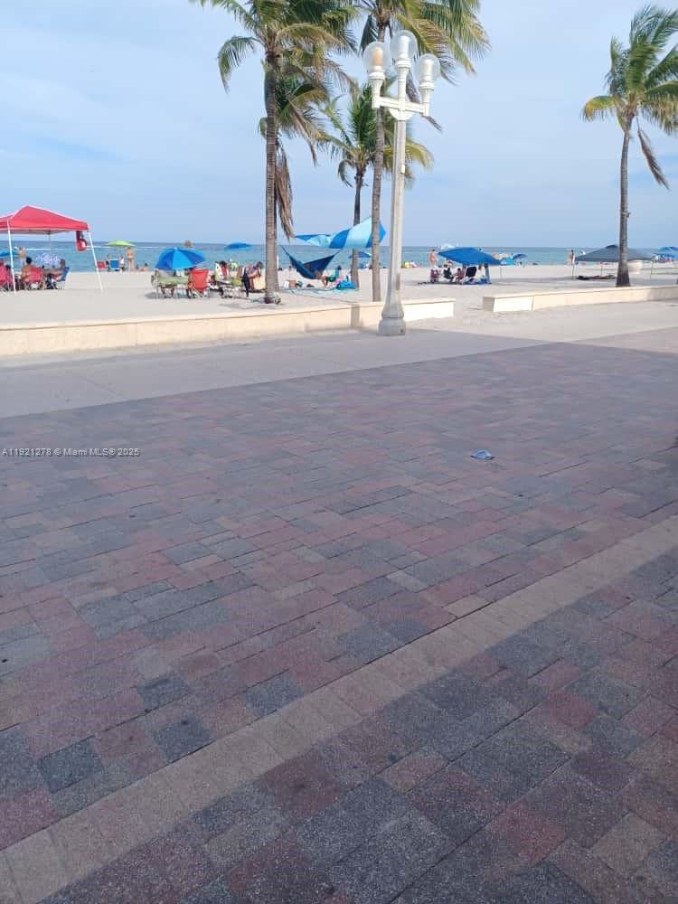 A paved boardwalk overlooks a sandy beach with palm trees, umbrellas, and the ocean — 322 Nebraska St # 1, Hollywood FL 33019, HOLLYWOOD, FL