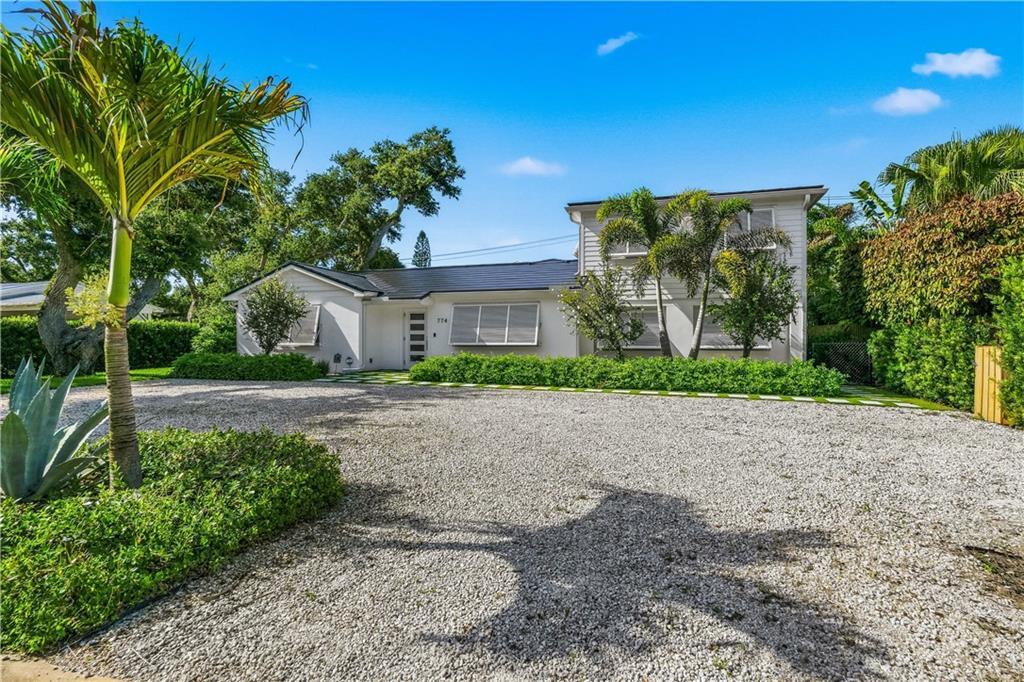 A two-story white house with a gravel driveway and palm trees under a blue sky — VERO BEACH, FL