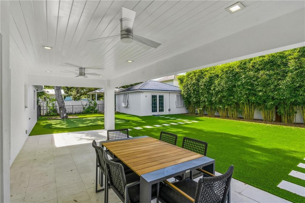 A covered patio with a dining set overlooks a backyard with artificial turf and landscaping — VERO BEACH, FL