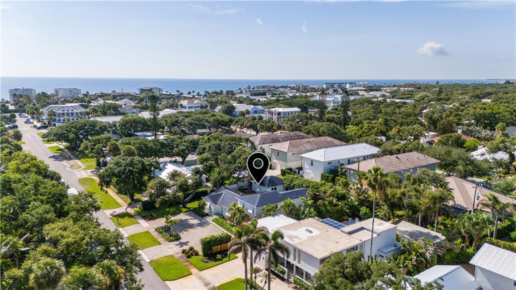 An aerial view shows a residential neighborhood with houses, lush trees, and the ocean beyond — VERO BEACH, FL