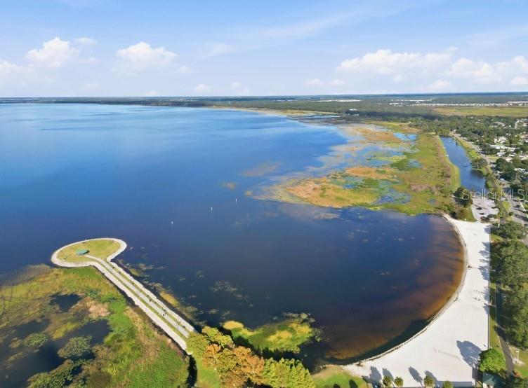 An aerial view of a lake with a sandy beach, a pier, and surrounding vegetation — 5123 CHATTAHOOCHEE BEND, ST CLOUD, FL