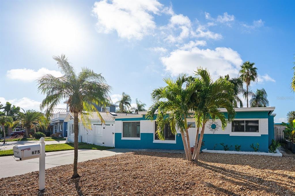 A teal and white single-story house features a gravel front yard and palm trees — 675 182ND AVENUE E, REDINGTON SHORES, FL
