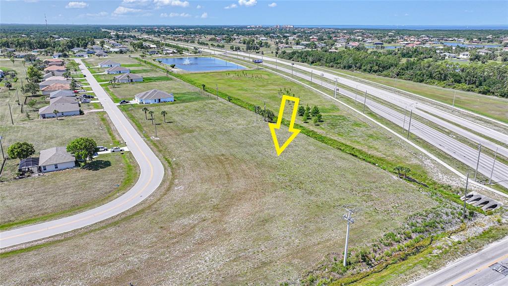 An aerial view shows a vacant grassy lot bordered by a road and a highway — 16035 BADALONA DRIVE, PUNTA GORDA, FL