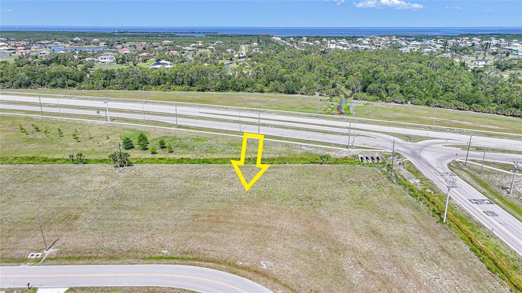 An aerial view shows a vacant, grassy lot situated near a highway and residential area — 16035 BADALONA DRIVE, PUNTA GORDA, FL