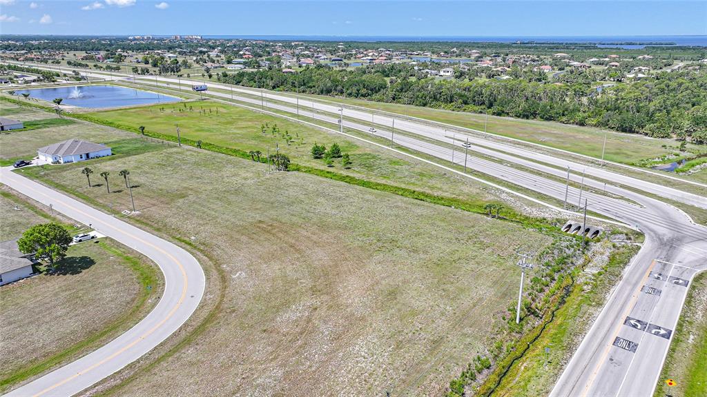 An aerial view shows a vacant grassy lot adjacent to a road and a highway — 16035 BADALONA DRIVE, PUNTA GORDA, FL
