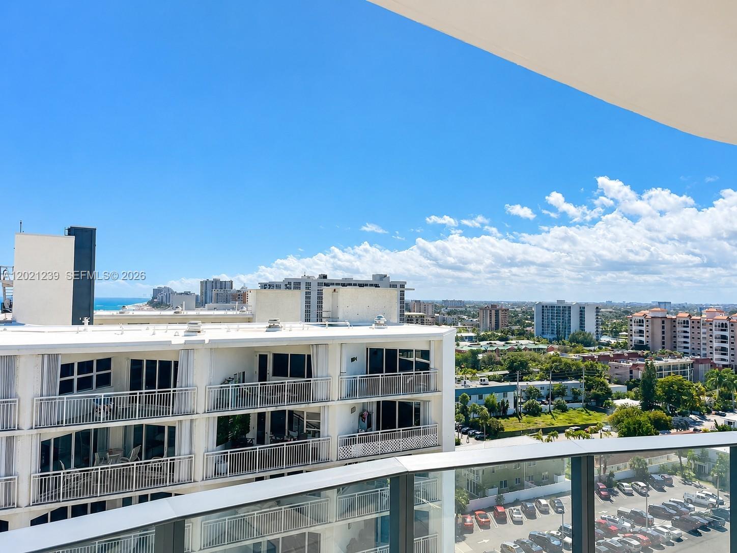 A high-angle view from a balcony overlooking a white apartment building and parking lot — 730 N Ocean Blvd # 1205, Pompano Beach FL 33062, POMPANO BEACH, FL