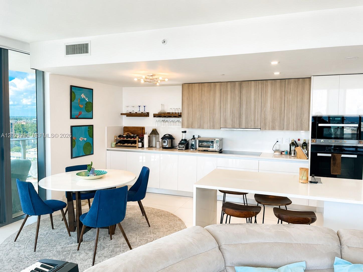 A modern kitchen features white cabinetry, wood-toned upper cabinets, a dining area, and a breakfast island — 730 N Ocean Blvd # 1205, Pompano Beach FL 33062, POMPANO BEACH, FL
