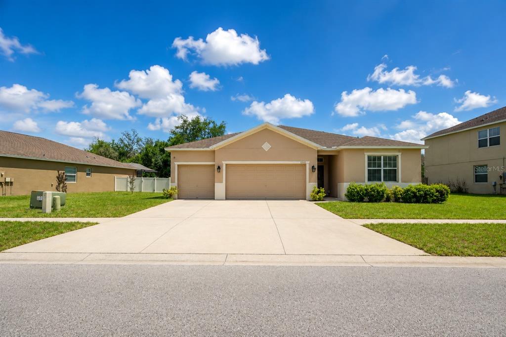 A single-story tan house with a three-car garage and a concrete driveway — 13842 BEE TREE COURT, HUDSON, FL