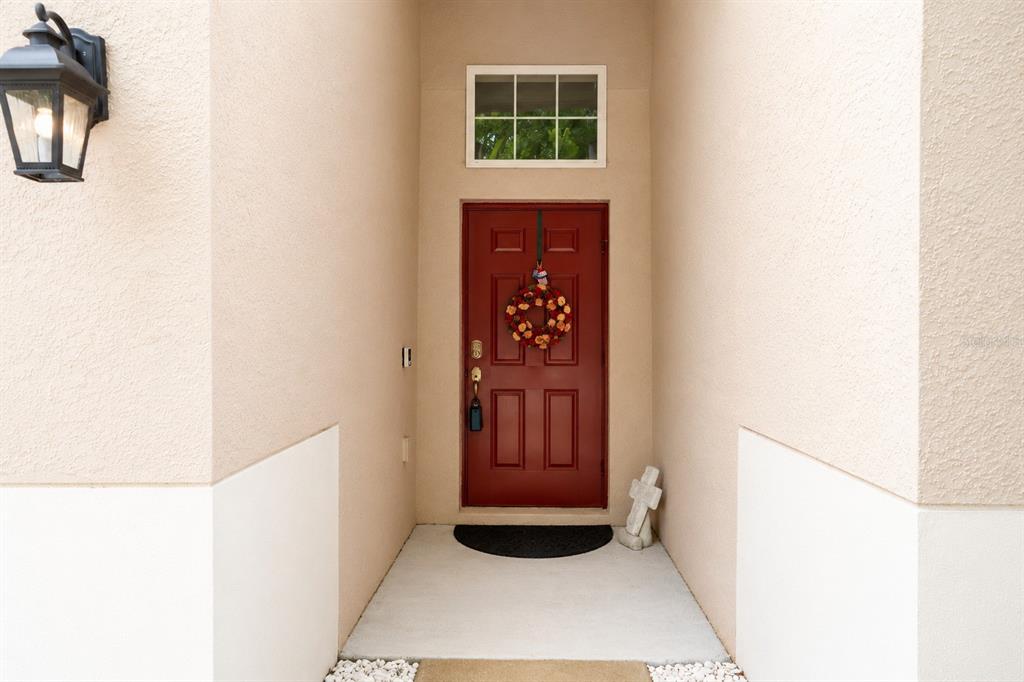 A red front door with a wreath is set within a recessed entryway — 13842 BEE TREE COURT, HUDSON, FL