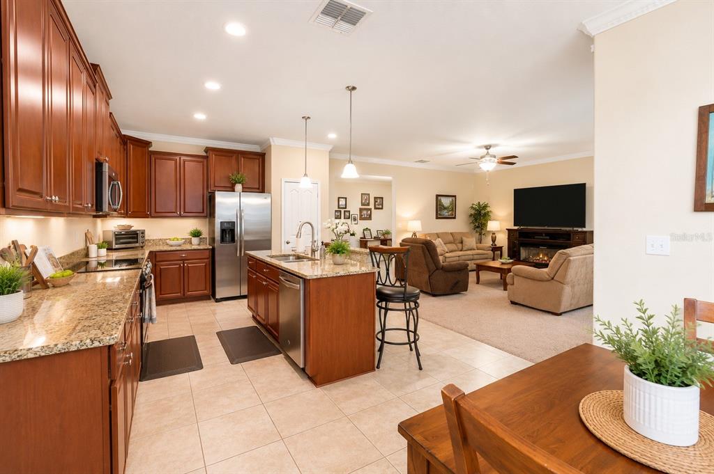 An open-concept kitchen with wood cabinets and granite countertops overlooks a carpeted living room — 13842 BEE TREE COURT, HUDSON, FL
