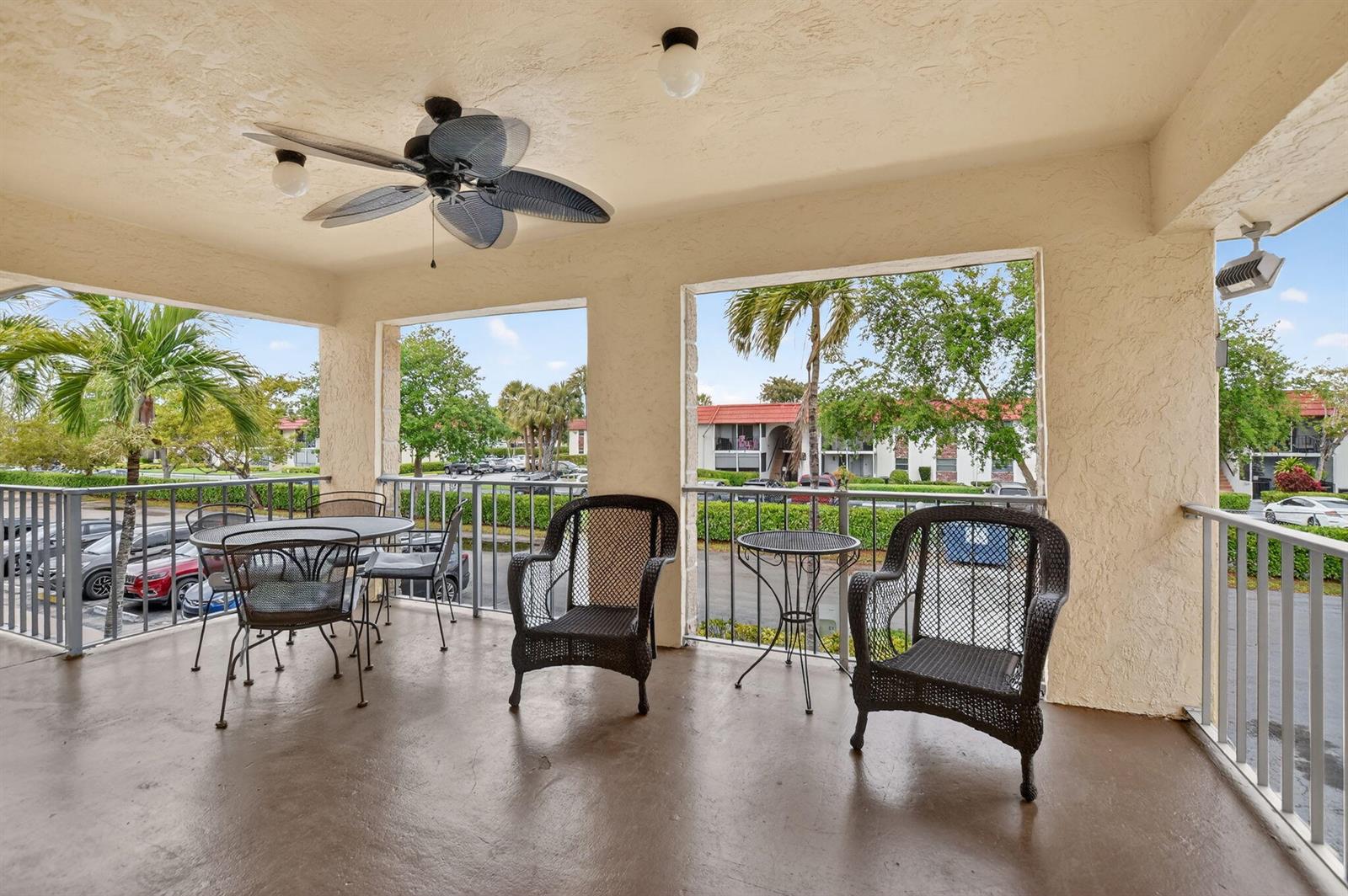 A covered balcony features a ceiling fan, wicker chairs, a dining set, and metal railings — 9855 Sandalfoot Boulevard Apt 317, Boca Raton FL 33428, BOCA RATON, FL