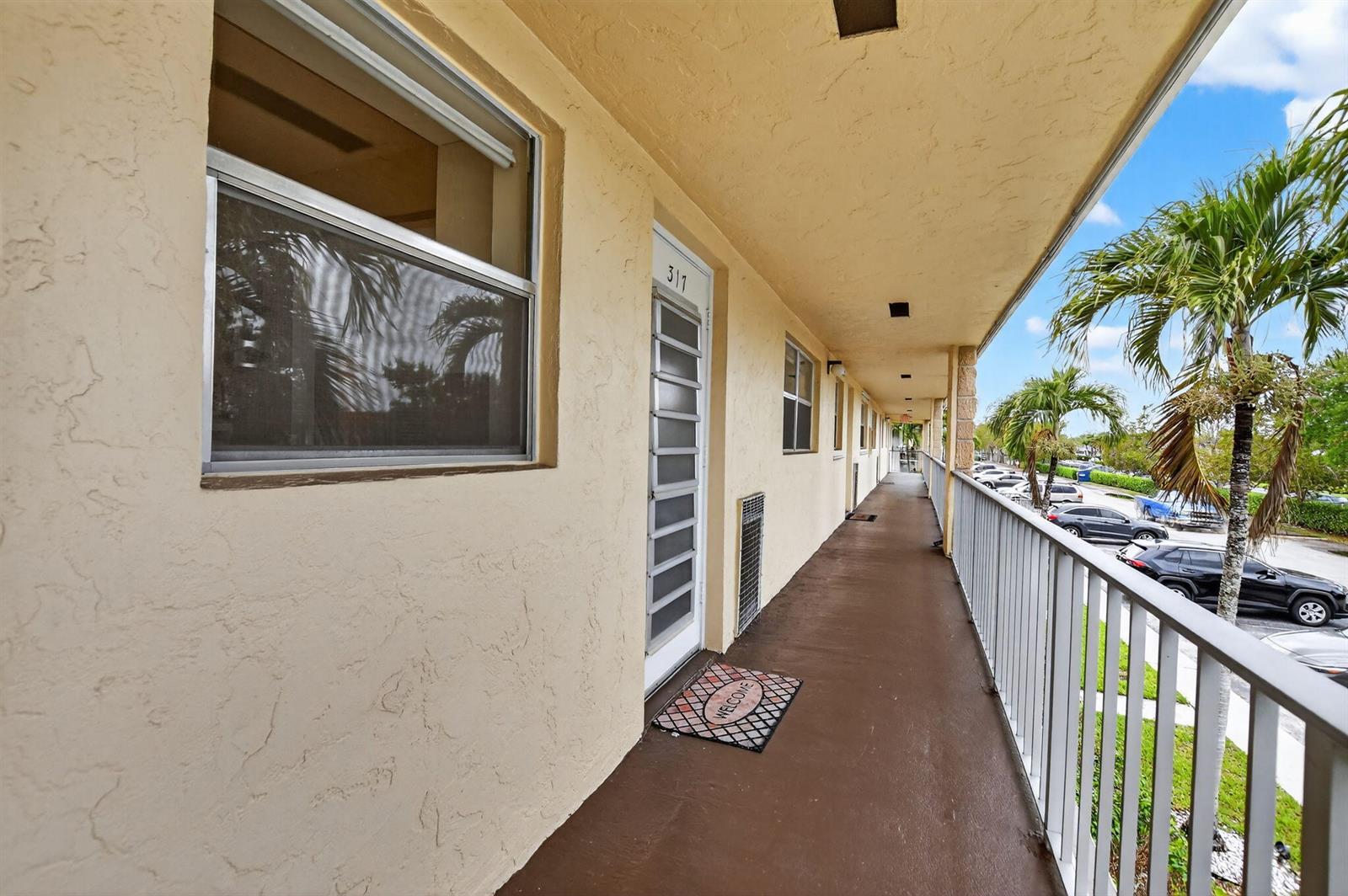 An exterior walkway with a white door, a welcome mat, and a metal railing — 9855 Sandalfoot Boulevard Apt 317, Boca Raton FL 33428, BOCA RATON, FL