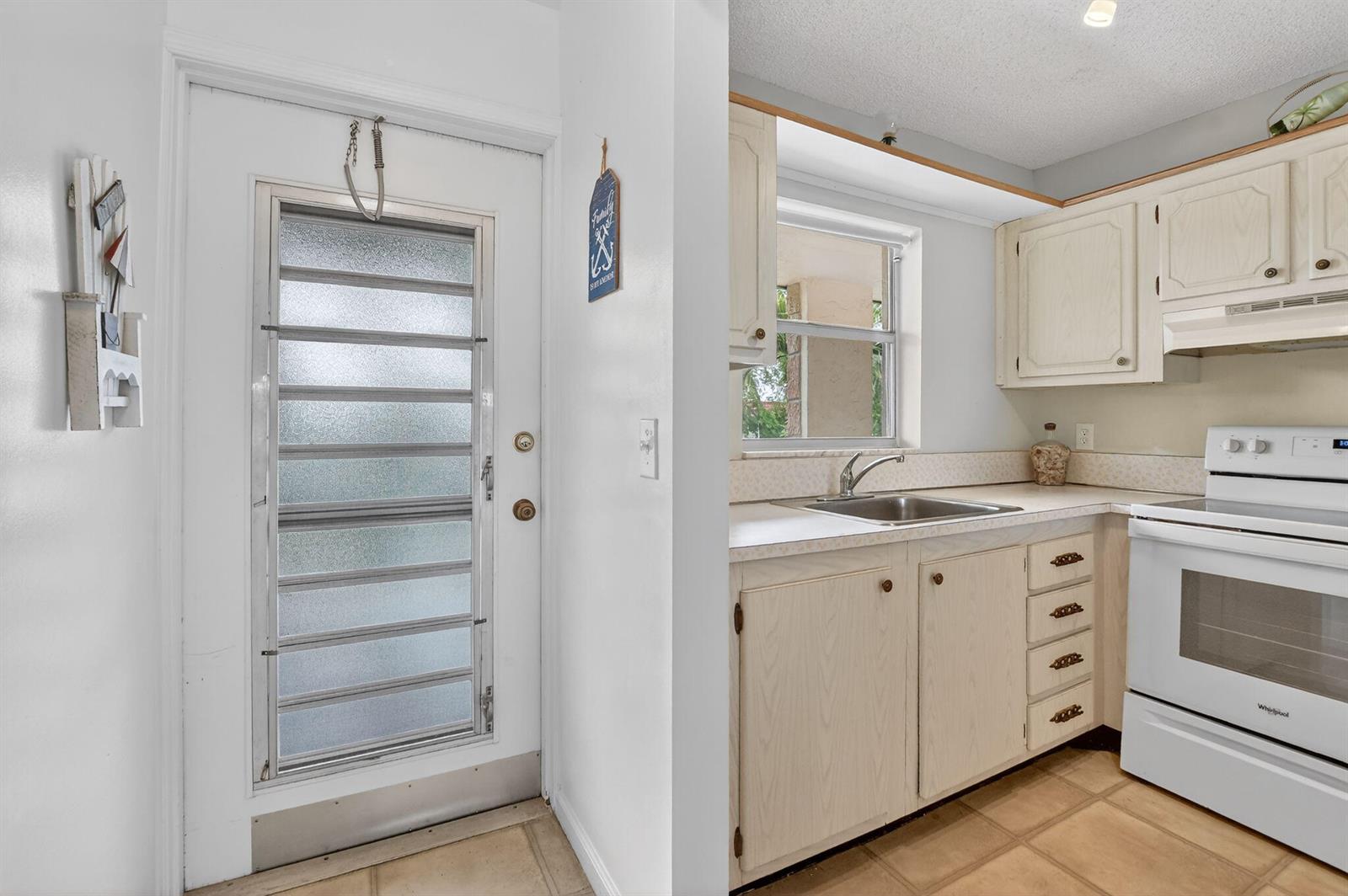 A white door with horizontal glass panels sits beside a kitchen with light-colored cabinets — 9855 Sandalfoot Boulevard Apt 317, Boca Raton FL 33428, BOCA RATON, FL