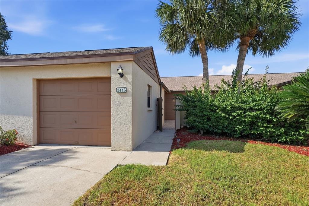 A single-story house exterior features a tan stucco facade, a brown garage door, and palm trees — 3446 BEEKMAN PLACE UNIT 50, SARASOTA, FL