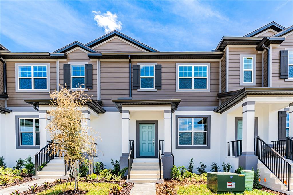 The exterior of a two-story townhouse featuring white stucco, gray siding, and a blue front door — 15811 TOLLINGTON ALLEY, WINTER GARDEN, FL