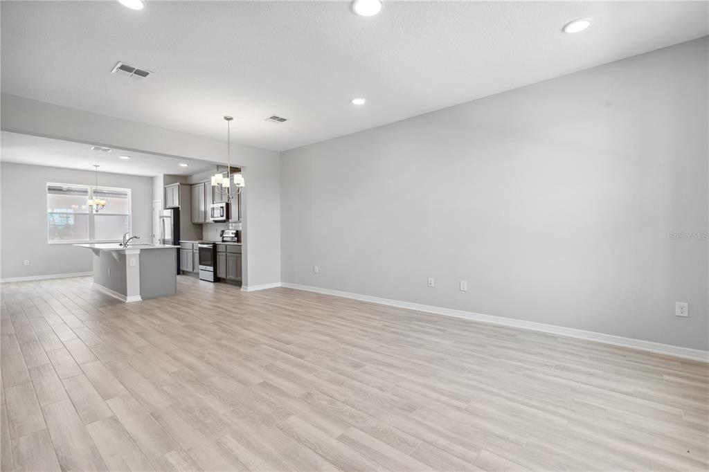 An open-concept living area with light wood-look tile flooring and a view into the kitchen — 15811 TOLLINGTON ALLEY, WINTER GARDEN, FL
