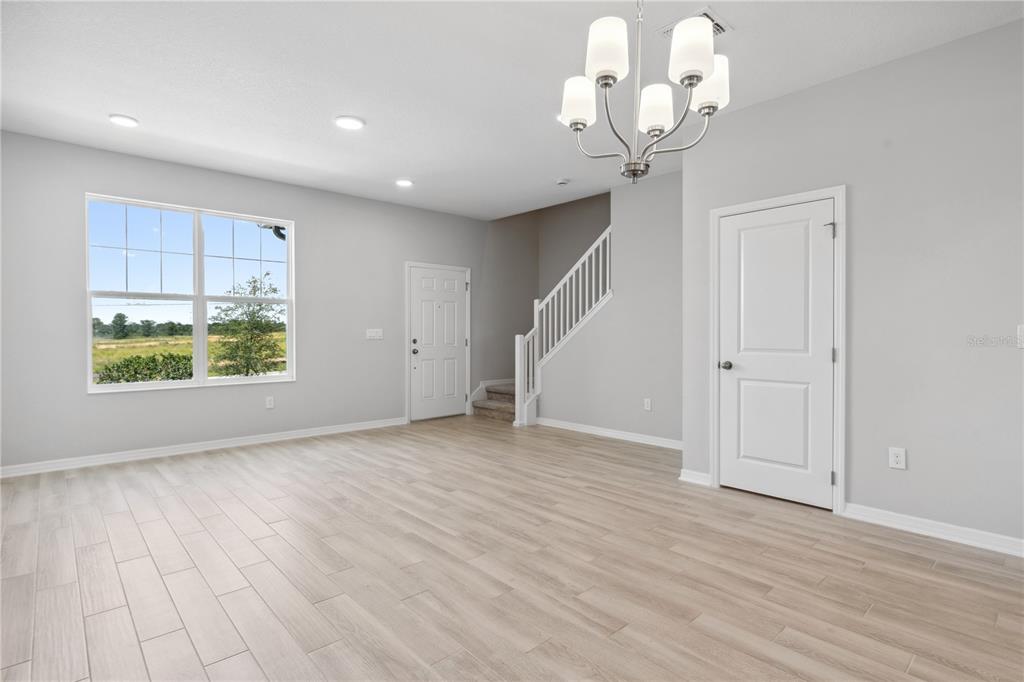 A bright, empty room features light wood-look flooring, a chandelier, a staircase, and a window — 15811 TOLLINGTON ALLEY, WINTER GARDEN, FL