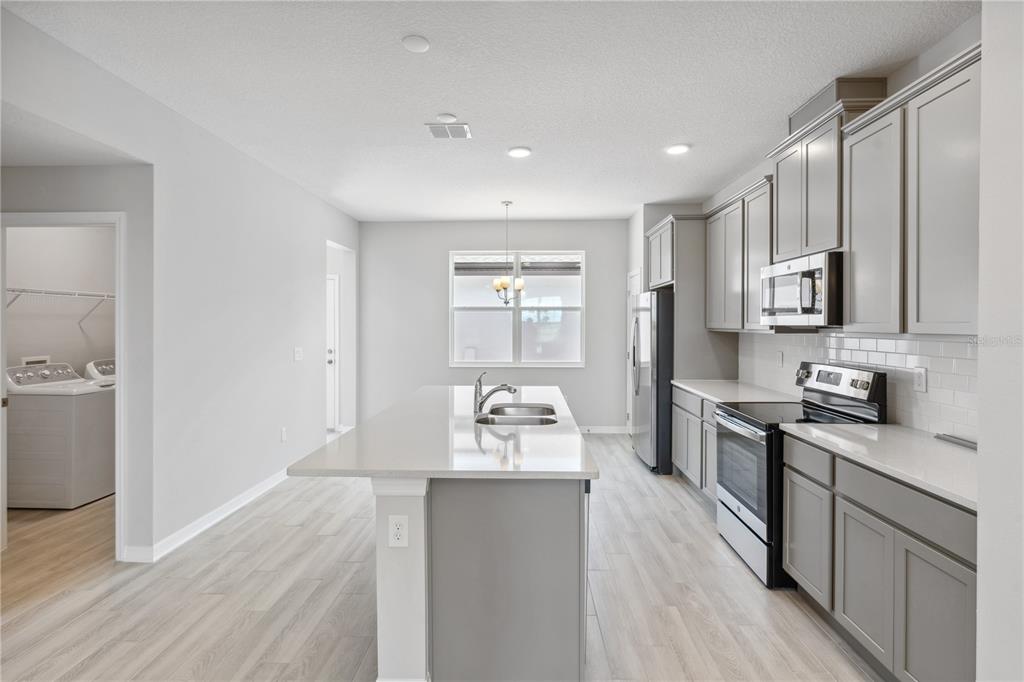A modern kitchen features gray cabinets, a central island with a sink, and light flooring — 15811 TOLLINGTON ALLEY, WINTER GARDEN, FL