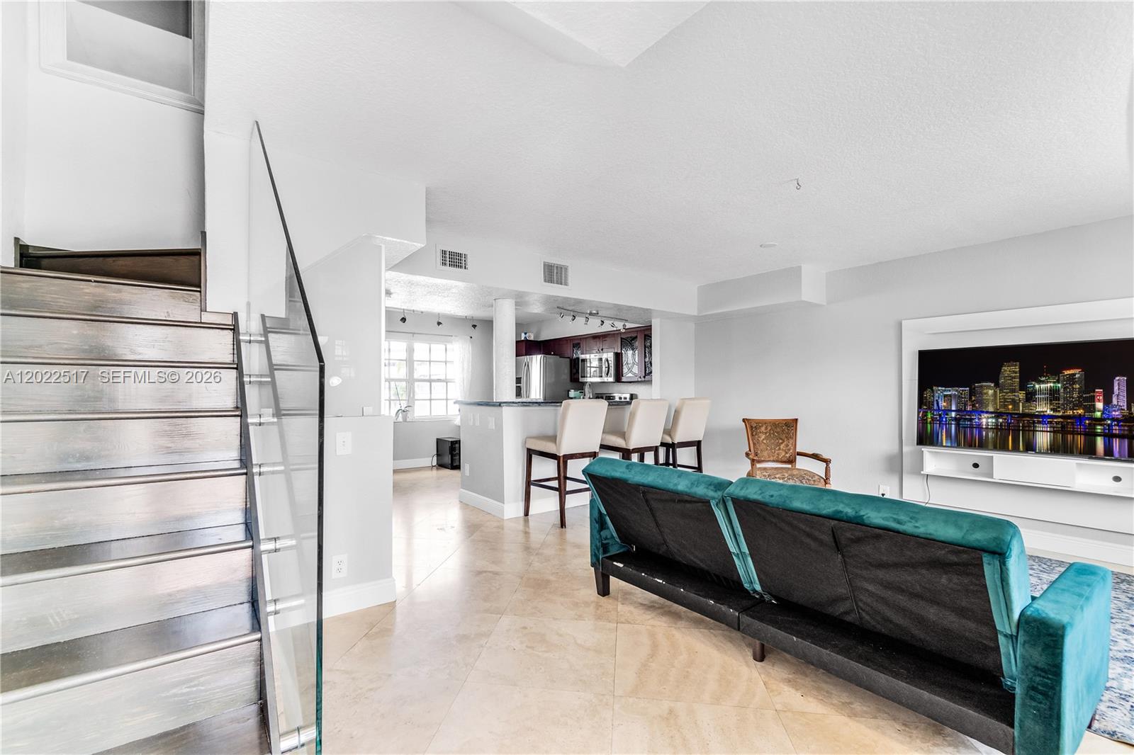 A living room with a staircase, kitchen area, and teal sofa faces a wall-mounted television — 349 Virginia St # 349, Hollywood FL 33019, HOLLYWOOD, FL