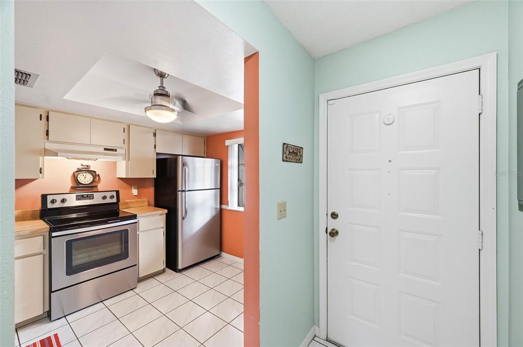 A kitchen with stainless steel appliances and white cabinets sits next to a white door — 7612 OAKMONT LANE, NEW PORT RICHEY, FL