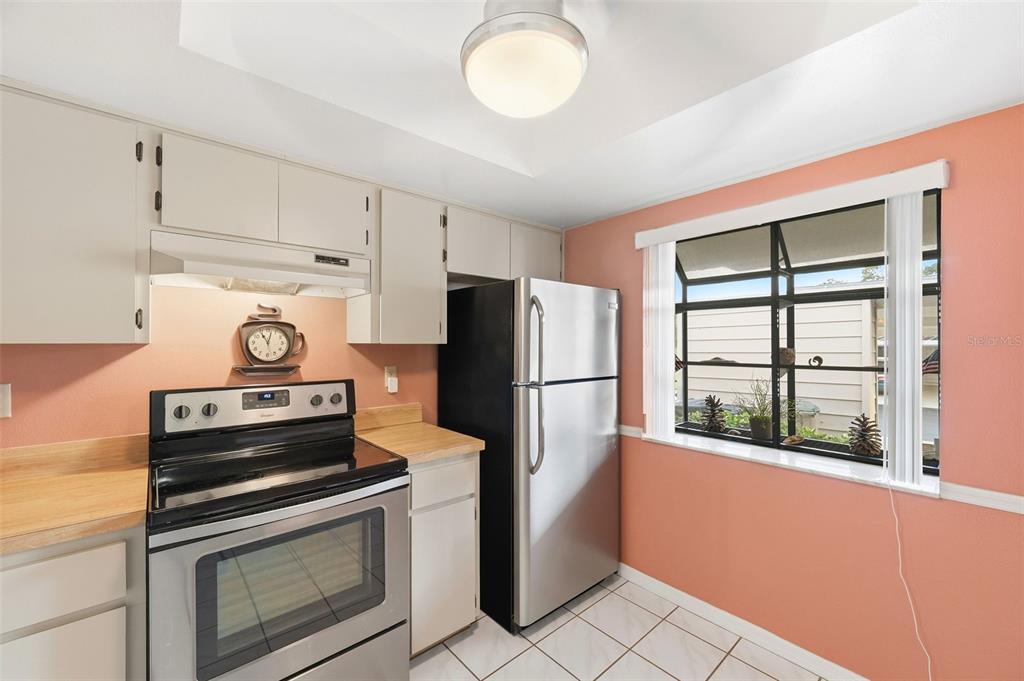 A kitchen features light-colored cabinets, a stainless steel stove and refrigerator, and peach-colored walls — 7612 OAKMONT LANE, NEW PORT RICHEY, FL