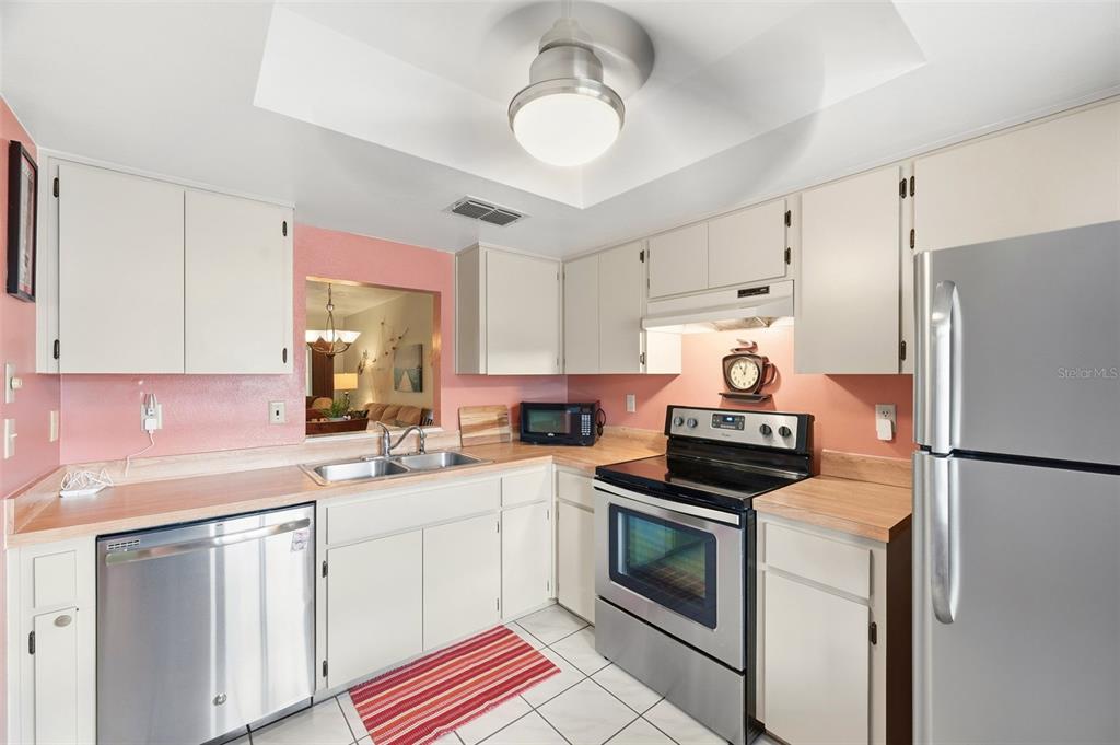 A kitchen with white cabinets, stainless steel appliances, pink walls, and light-colored countertops — 7612 OAKMONT LANE, NEW PORT RICHEY, FL
