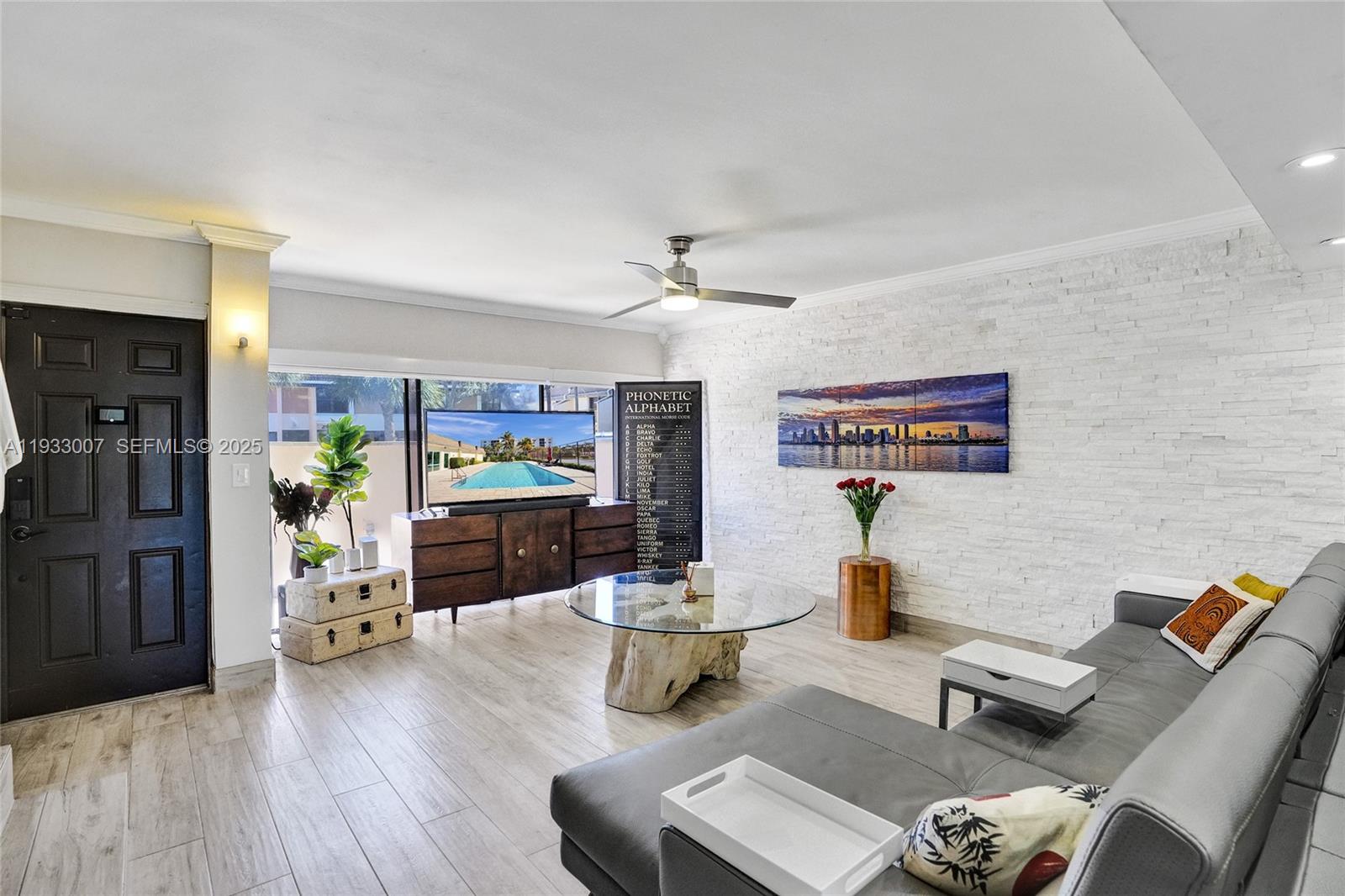 A living room features a grey sectional sofa, a glass coffee table, and a stone wall — 16478 NE 27th Pl # 34, Eastern Shores FL 33160, EASTERN SHORES, FL