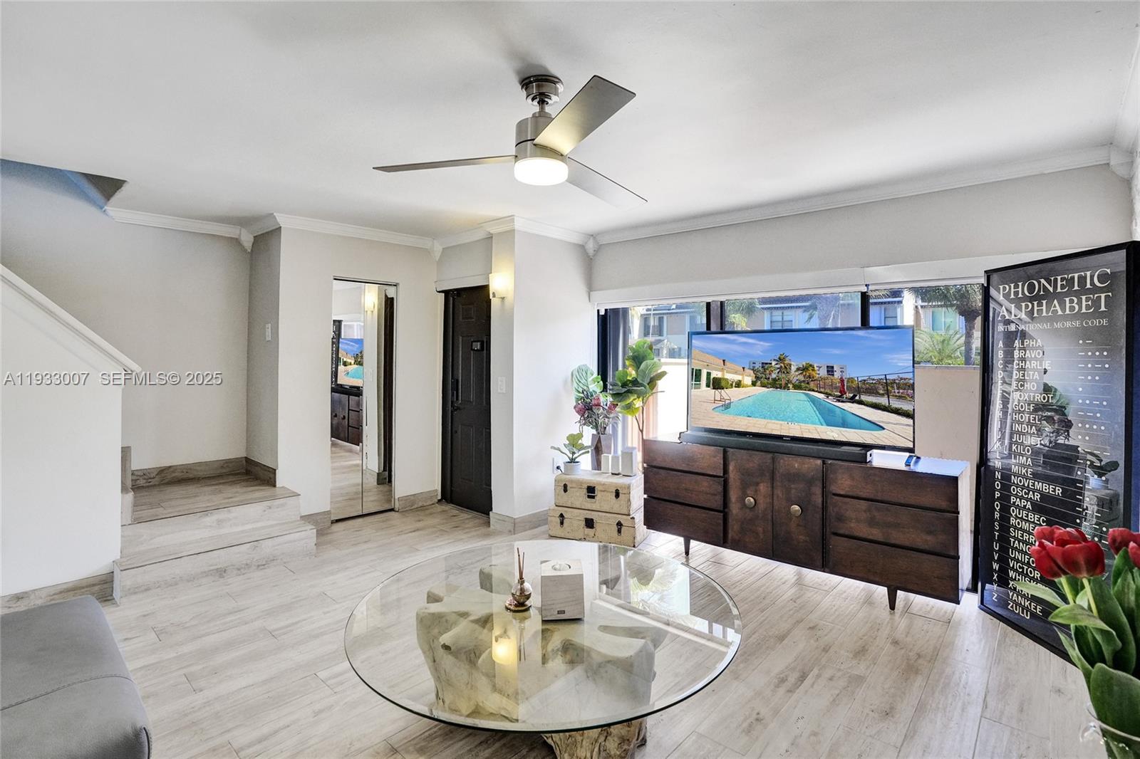 A living room features light wood-look flooring, a glass coffee table, and a television console — 16478 NE 27th Pl # 34, Eastern Shores FL 33160, EASTERN SHORES, FL