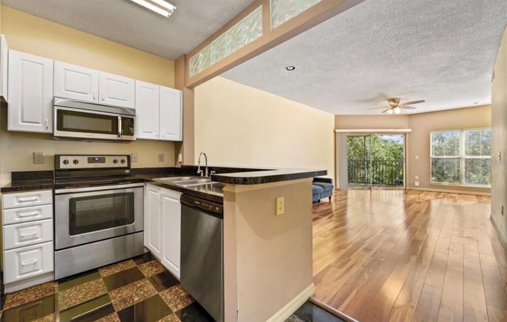 A kitchen with white cabinets and stainless steel appliances overlooks a living area with wood floors — 4107 CHATHAM OAK COURT UNIT 326, TAMPA, FL