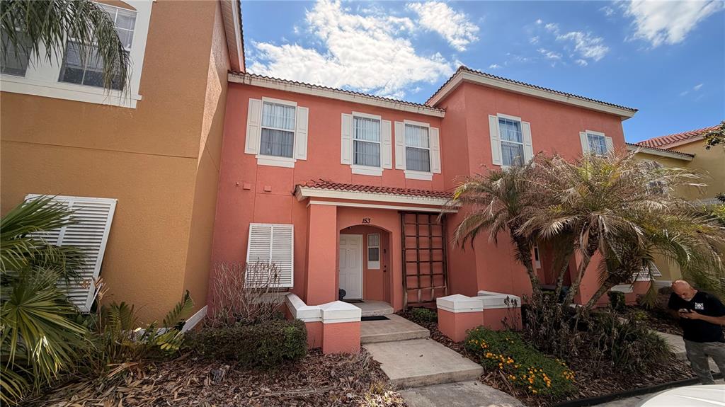 A two-story peach-colored townhouse features a white front door and a small palm tree — 153 POMPANO BEACH DR DRIVE, KISSIMMEE, FL