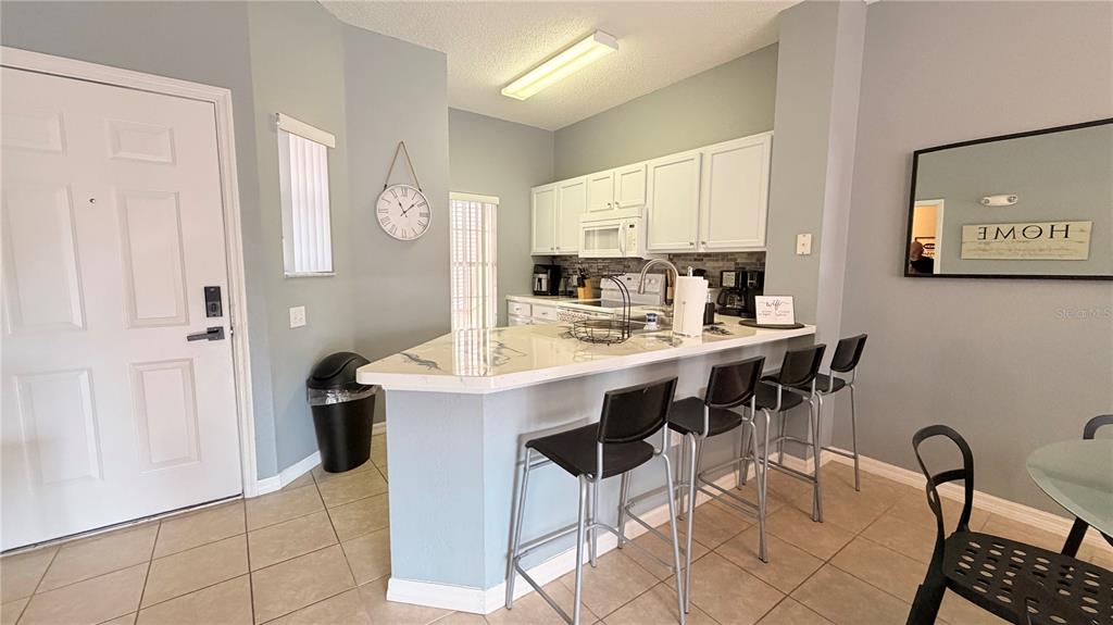 A kitchen features white cabinets, a breakfast bar with four stools, and tile flooring — 153 POMPANO BEACH DR DRIVE, KISSIMMEE, FL