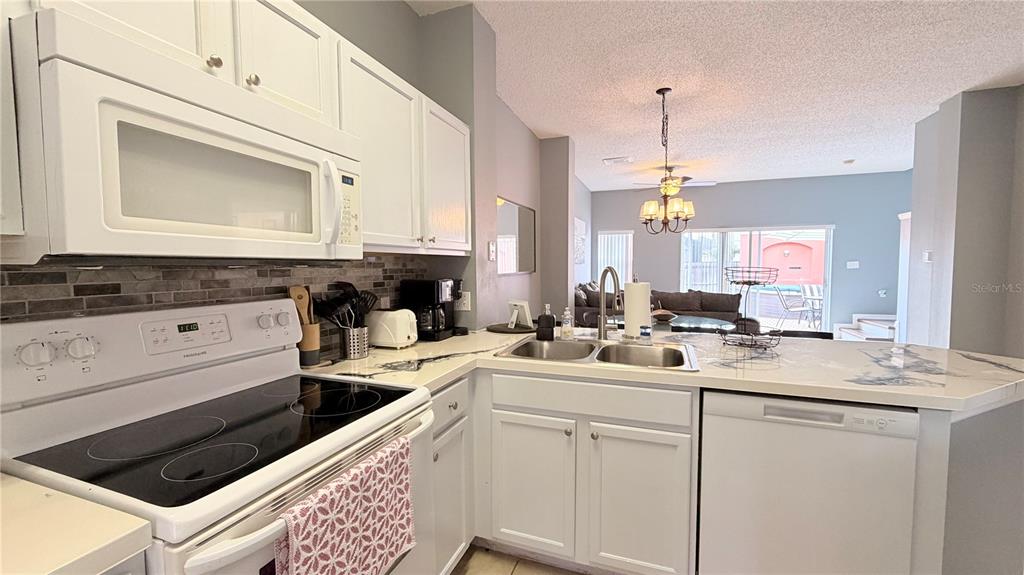 A kitchen features white cabinets, a glass-top stove, a double sink, and a breakfast bar — 153 POMPANO BEACH DR DRIVE, KISSIMMEE, FL