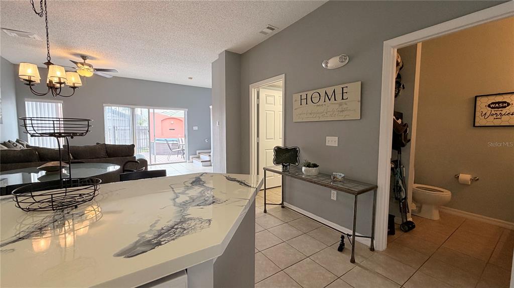 A kitchen counter overlooks a living area with a sliding glass door and a bathroom — 153 POMPANO BEACH DR DRIVE, KISSIMMEE, FL