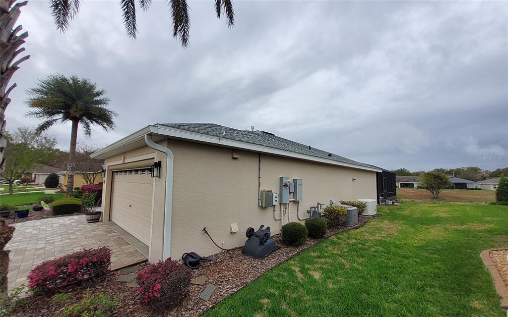 The exterior side view of a house shows a garage, electrical equipment, and landscaping — 26657 MANASSAS DRIVE, LEESBURG, FL