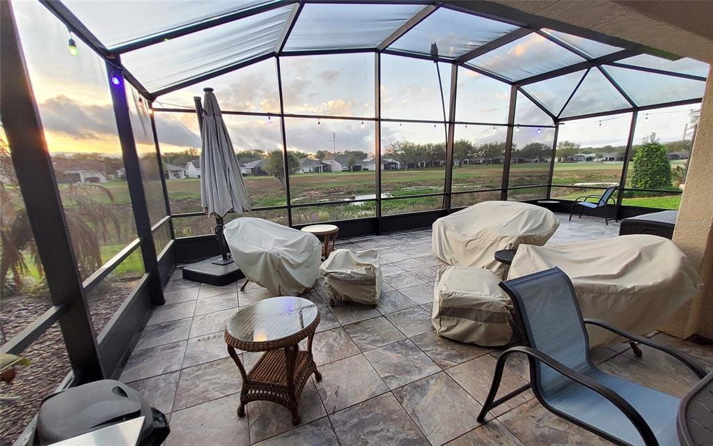 A screened-in patio features tiled flooring, covered outdoor furniture, and a view of a pond — 26657 MANASSAS DRIVE, LEESBURG, FL
