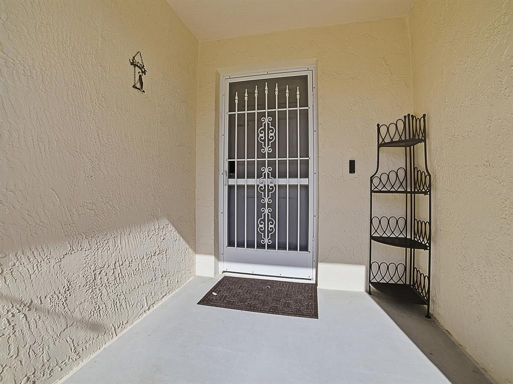 A covered entryway features a white security screen door, a dark metal shelf, and a mat — 1202 FERNANDO LANE, LADY LAKE, FL