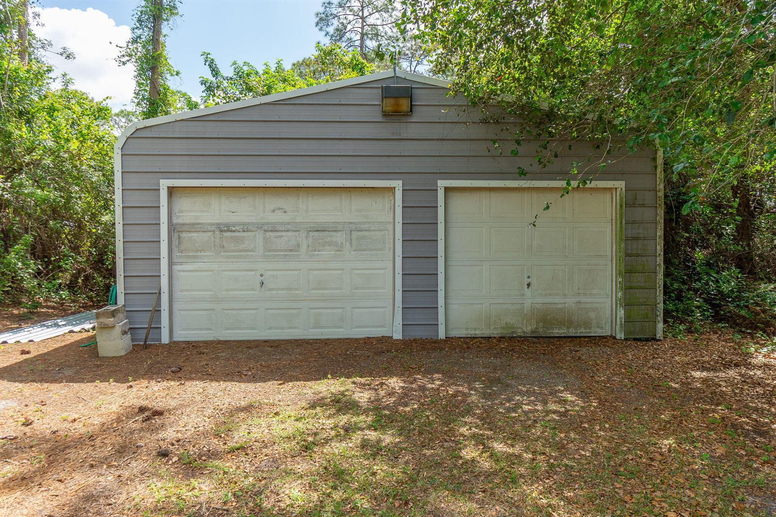A detached metal garage with two white roll-up doors sits on a wooded lot — 15578 89th Place N, Loxahatchee FL 33470, LOXAHATCHEE, FL