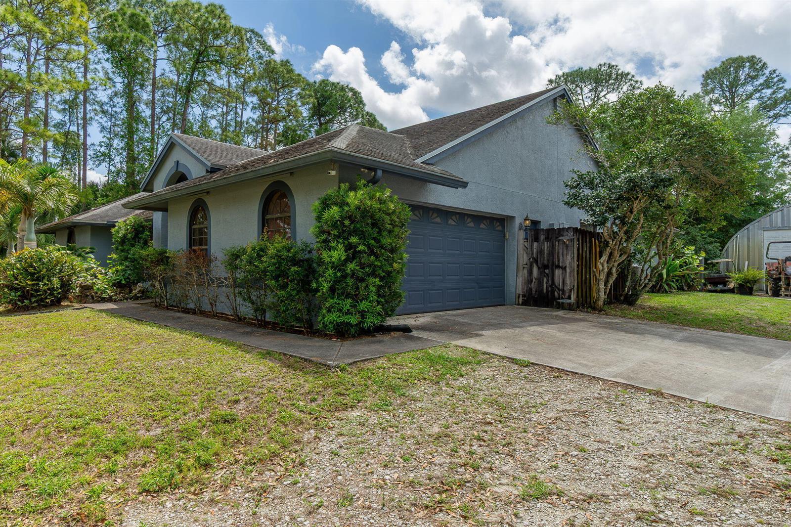 A gray house with a two-car garage and arched windows sits on a gravel driveway — 15578 89th Place N, Loxahatchee FL 33470, LOXAHATCHEE, FL
