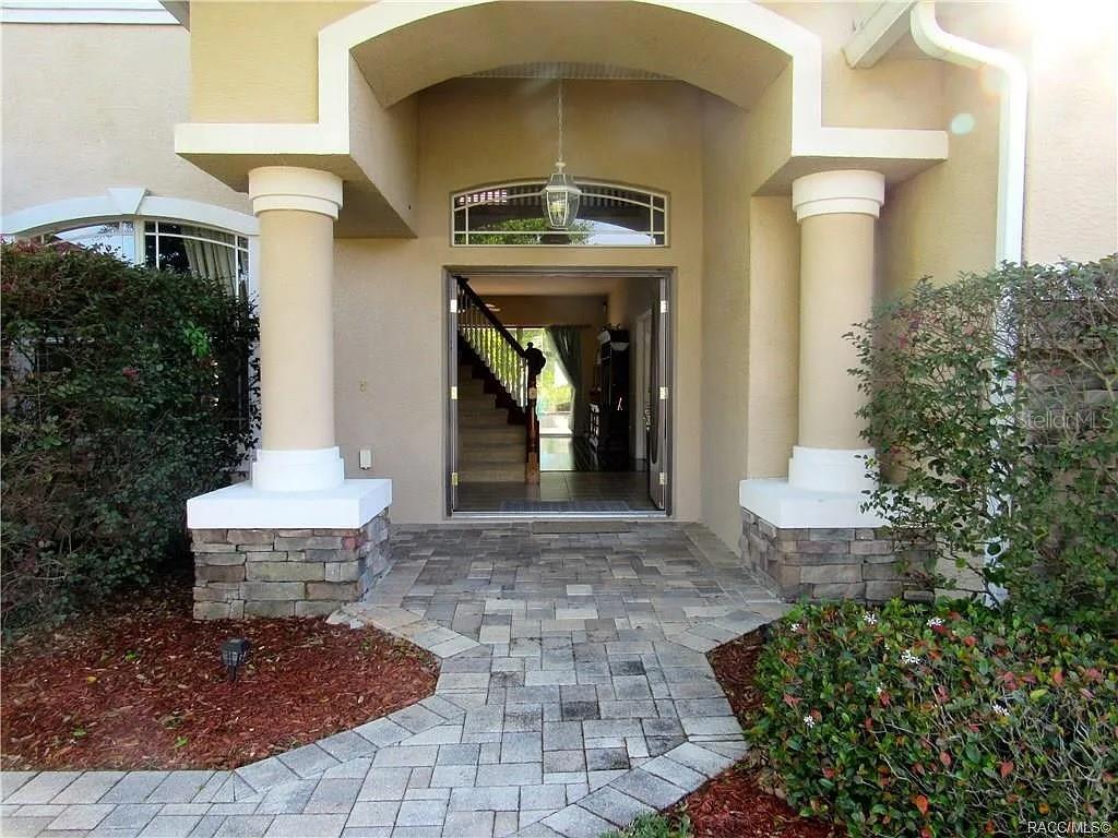 The front entrance features a paved walkway, two columns, and double doors with oval glass inserts — 13038 PASTORE COURT, SPRING HILL, FL