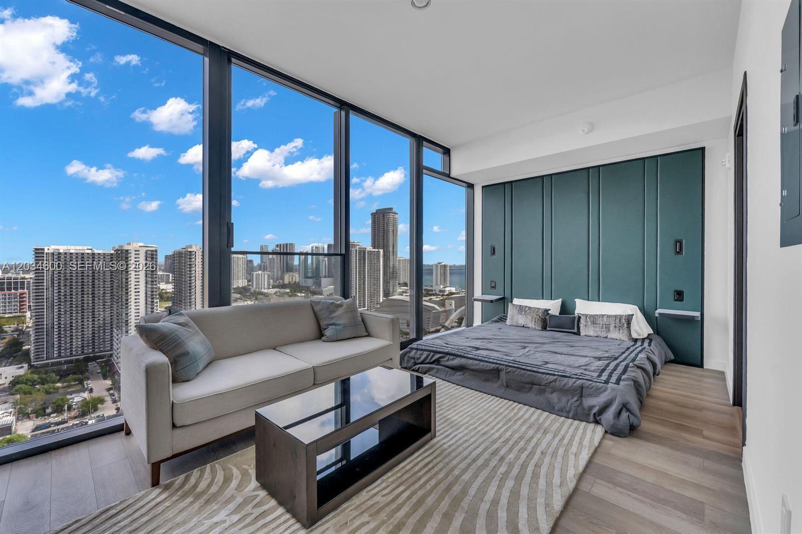 A modern bedroom features floor-to-ceiling windows, a low-profile bed, and a teal upholstered headboard — 20 NE 11th ST # 2803A, Miami FL 33132, MIAMI, FL