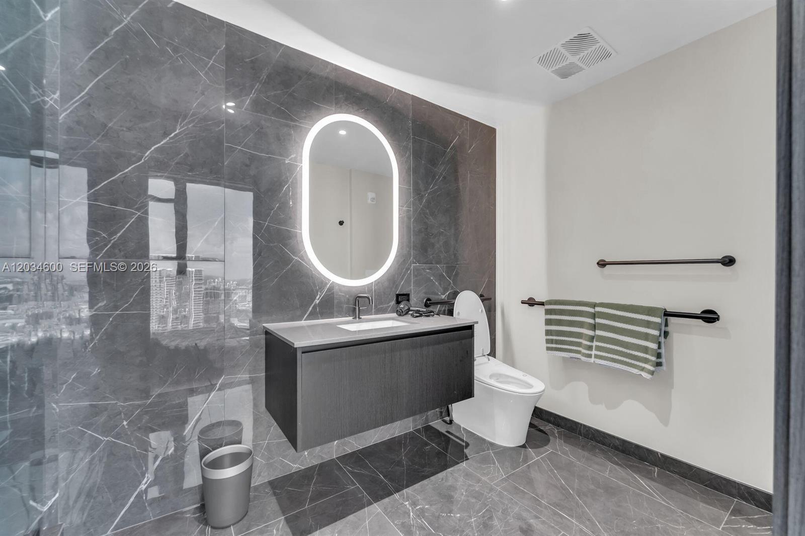 A modern bathroom features dark marble walls, a floating vanity, and an illuminated oval mirror — 20 NE 11th ST # 2803A, Miami FL 33132, MIAMI, FL