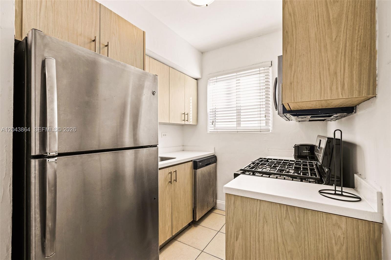 A kitchen features light wood cabinets, stainless steel appliances, and white countertops — 7340 Harding Ave # 16, Miami Beach FL 33141, MIAMI BEACH, FL