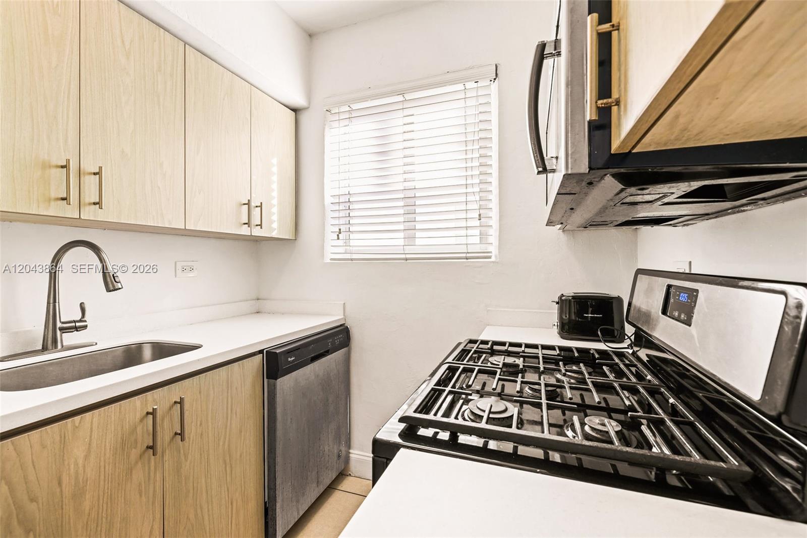 A galley kitchen features light wood cabinets, white countertops, a gas stove, and a dishwasher — 7340 Harding Ave # 16, Miami Beach FL 33141, MIAMI BEACH, FL