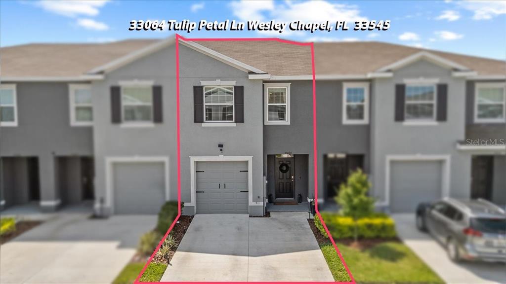 A two-story townhouse exterior features a gray facade, a single-car garage, and a concrete driveway — 33064 TULIP PETAL LANE, WESLEY CHAPEL, FL