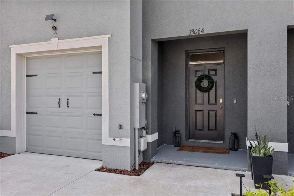 A gray exterior features a single-car garage and a recessed front door with a wreath — 33064 TULIP PETAL LANE, WESLEY CHAPEL, FL