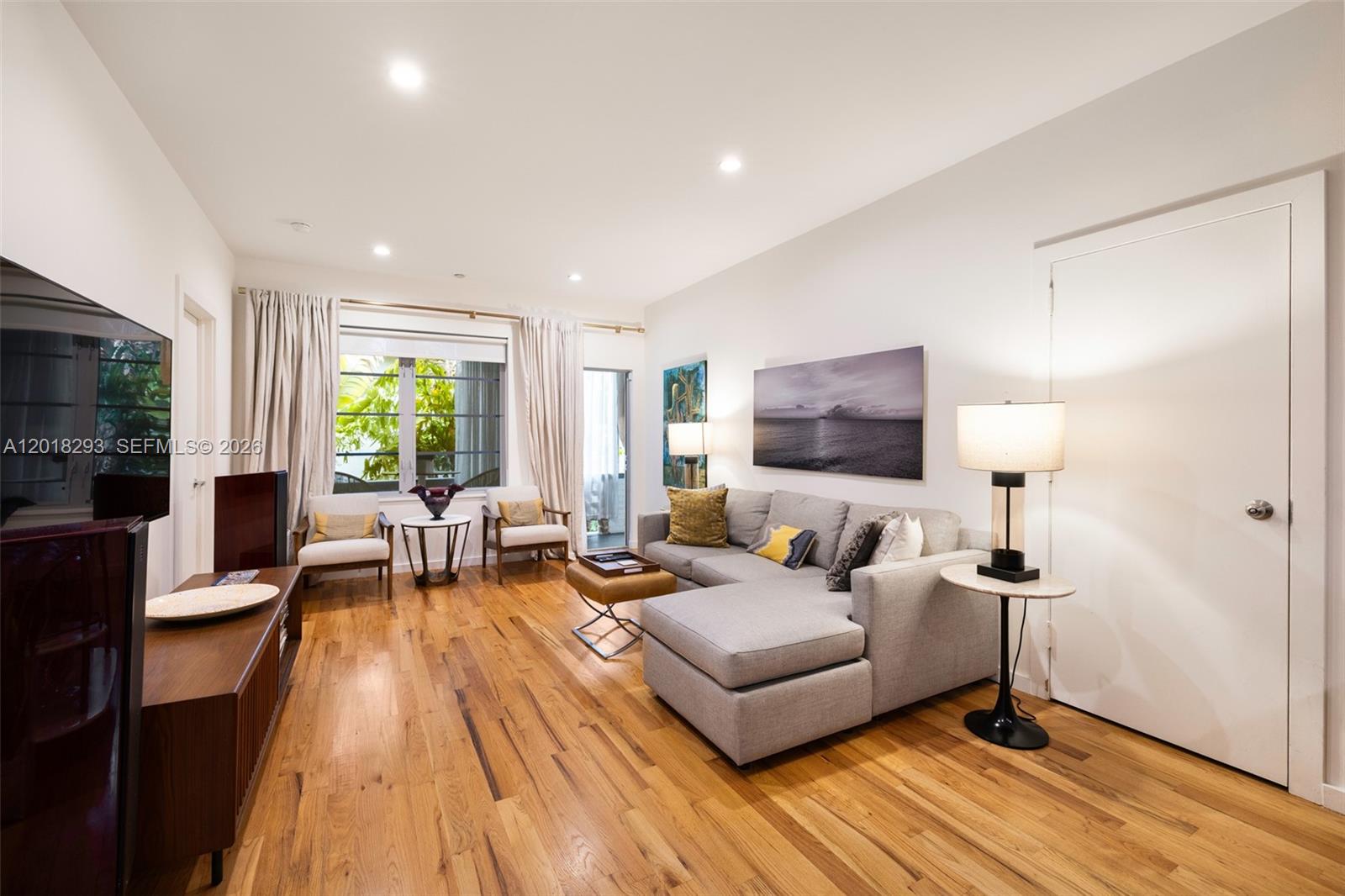 A living room features hardwood floors, a gray sectional sofa, and a large window — 1551 Lenox Ave # 8, Miami Beach FL 33139, MIAMI BEACH, FL
