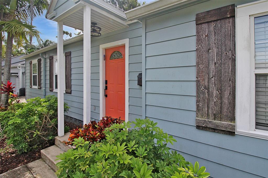 A light blue house exterior features a bright orange front door and rustic wooden shutters — 2321 18TH AVENUE W, BRADENTON, FL