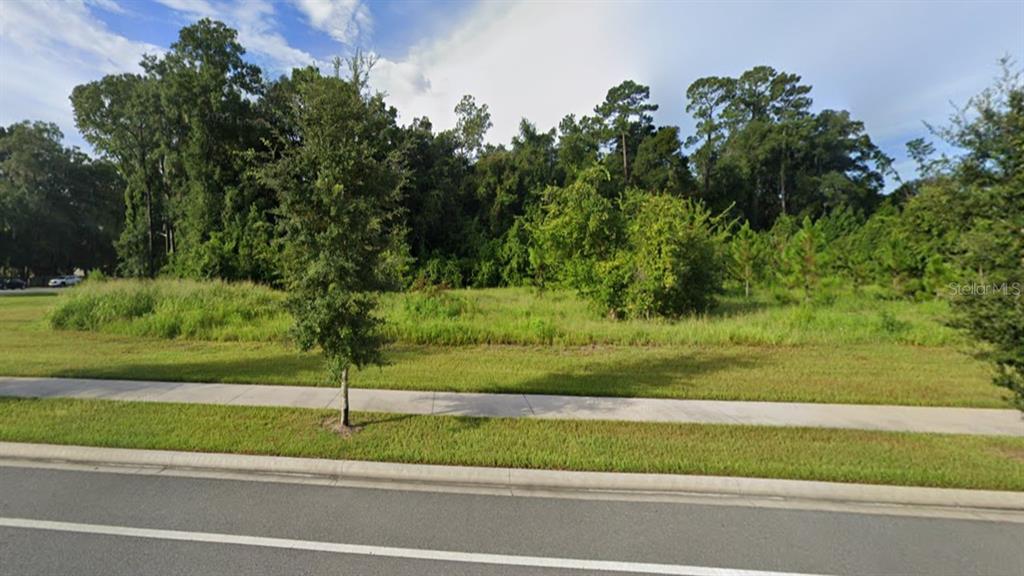 A vacant, grassy lot with a sidewalk and trees sits beside a paved road — TBD SW 24TH AVENUE, GAINESVILLE, FL