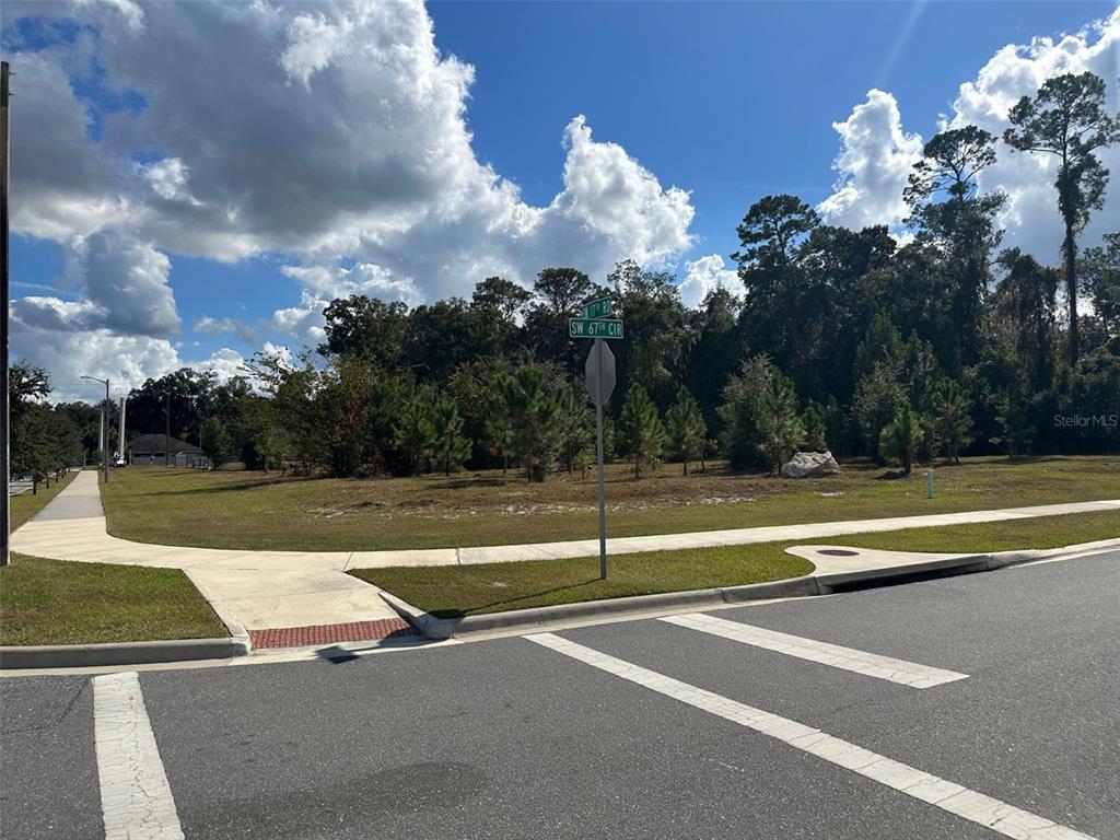 A vacant corner lot with a sidewalk and street sign under a cloudy blue sky — TBD SW 24TH AVENUE, GAINESVILLE, FL