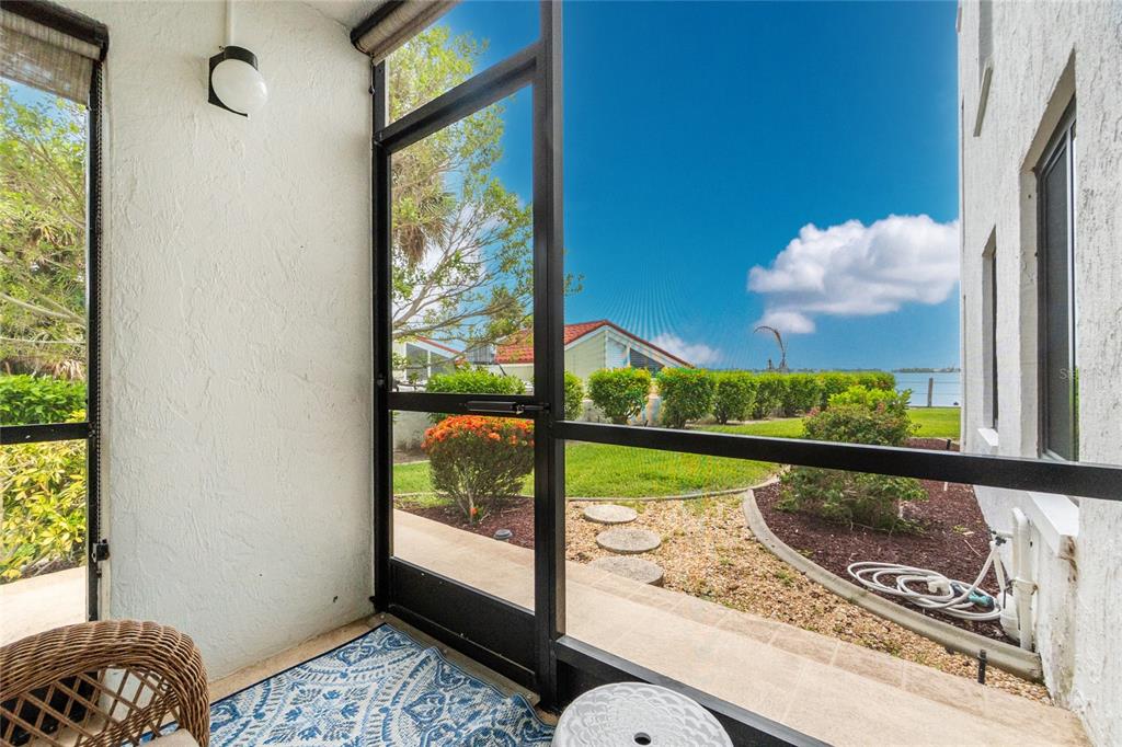 A screened-in porch overlooks a grassy yard, landscaping, and a distant view of the water — 2955 N BEACH ROAD UNIT A411, ENGLEWOOD, FL